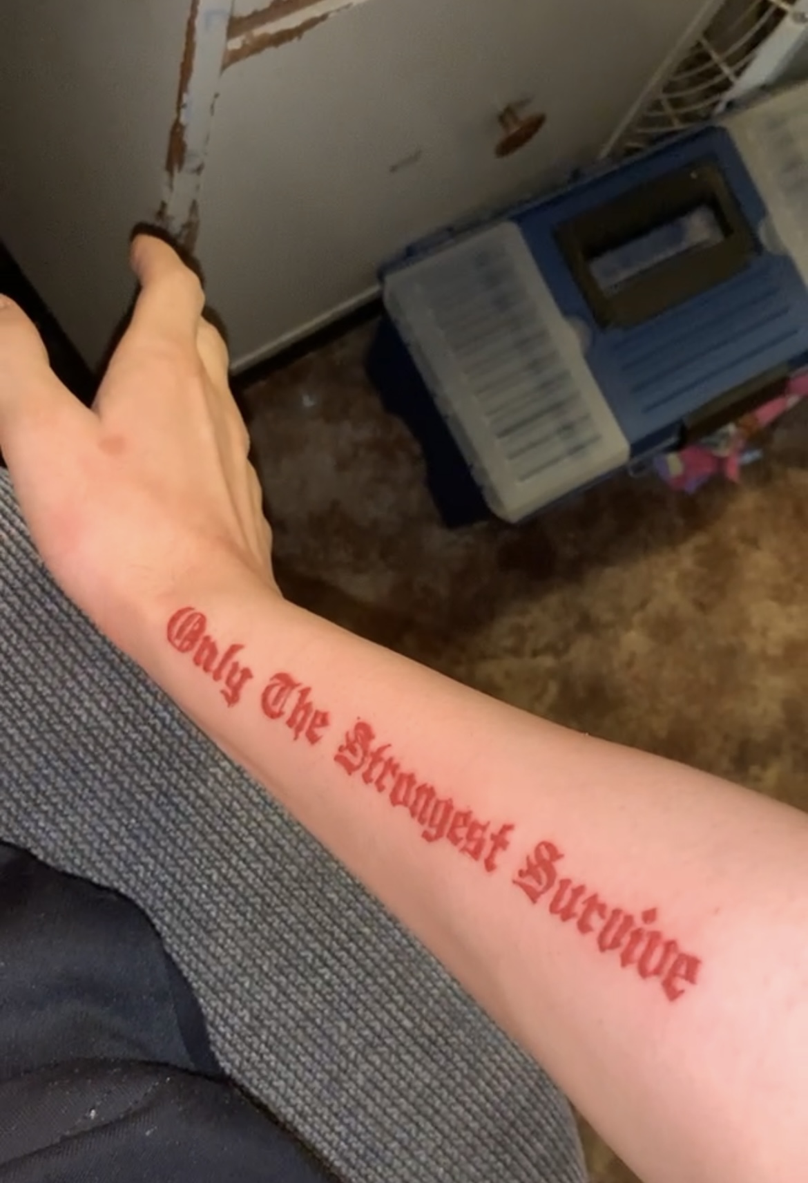 Que's tattoo — Only The Strongest Survive — in red ink